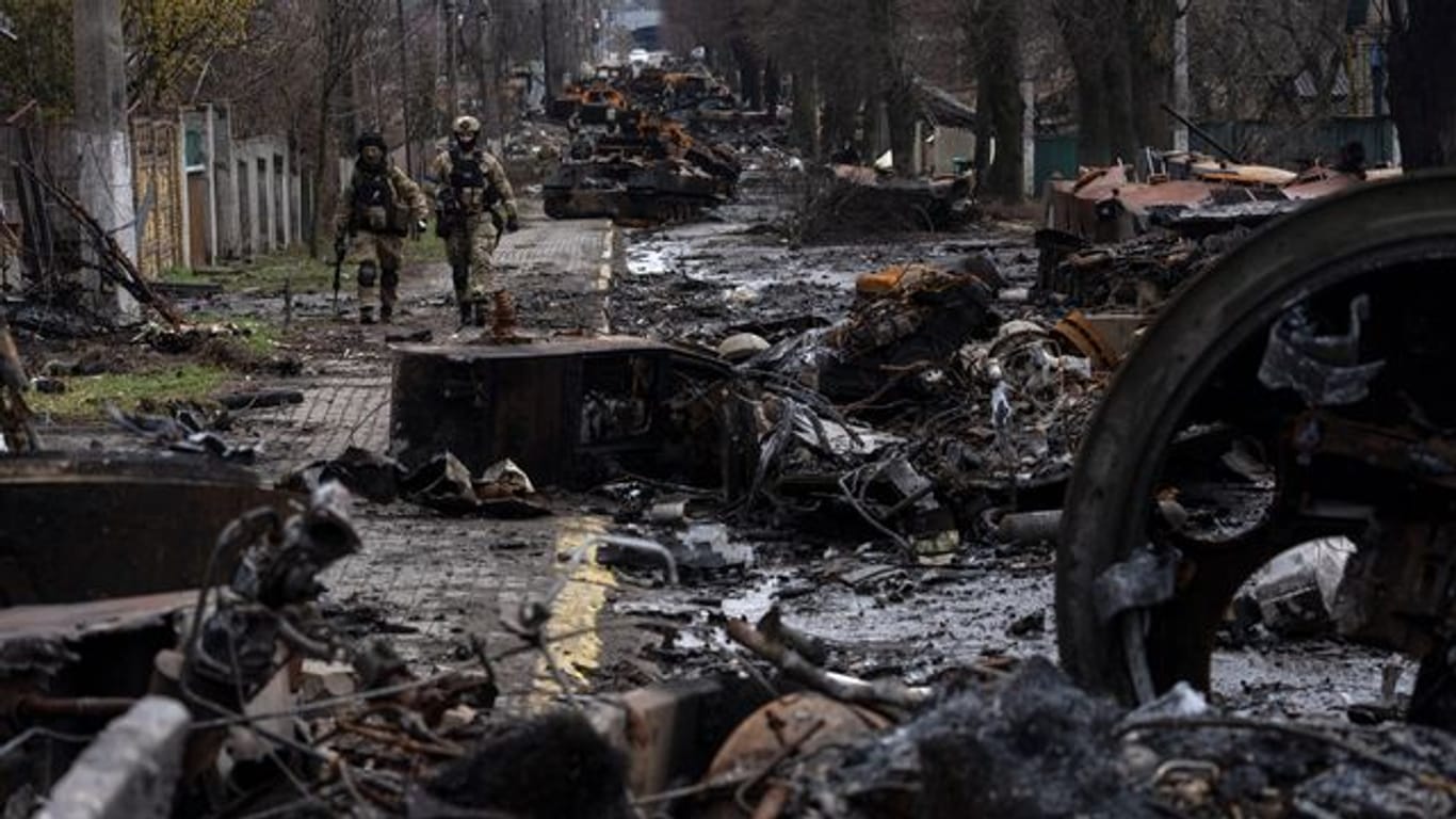 Zwei ukrainische Soldaten inspizieren in Butscha eine mit zerstörten russischen Militärfahrzeugen übersäte Straße.