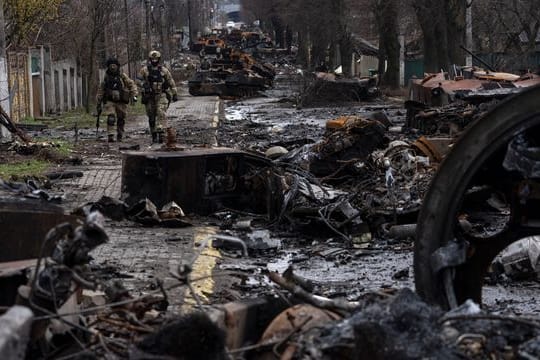 Zwei ukrainische Soldaten inspizieren in Butscha eine mit zerstörten russischen Militärfahrzeugen übersäte Straße.