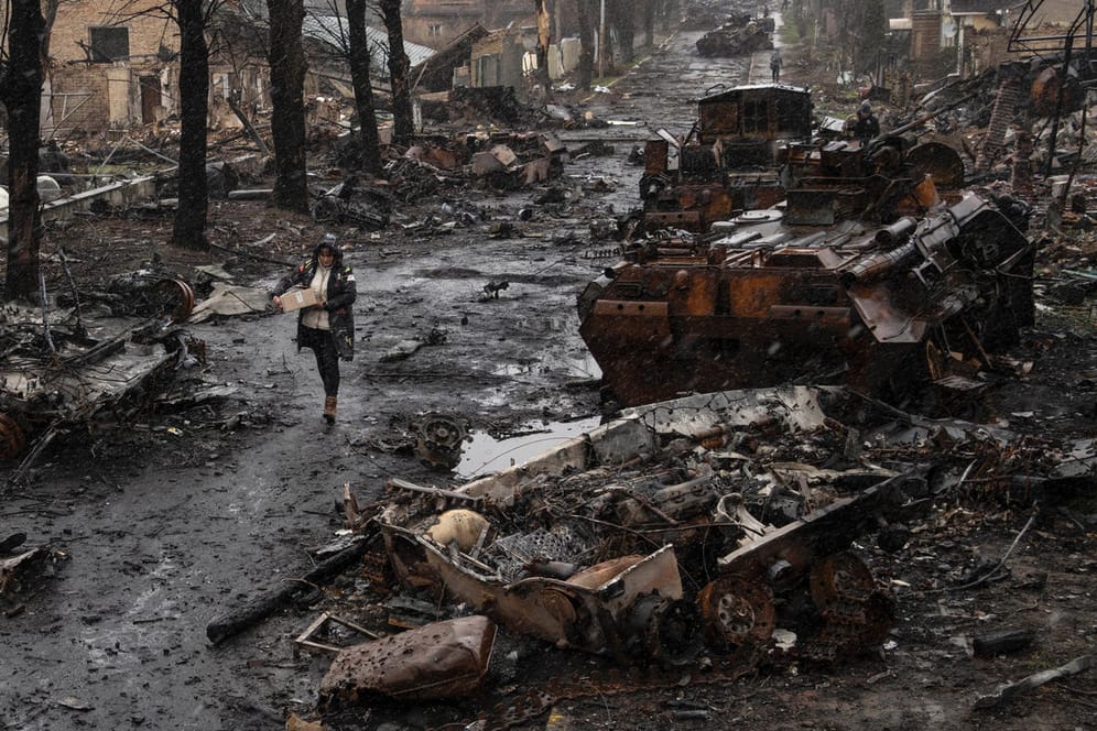 Eine Frau geht auf einer Straße, die übersät ist mit zerstörten russischen Militärfahrzeugen.