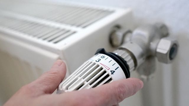 Eine Frau dreht an einem Heizungsthermostat.