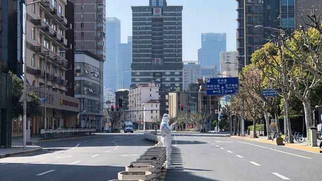 Ein Mann in einem Schutzanzug steht inmitten leerer Straßen in einem abgesperrten Gebiet im Bezirk Jingan im Westen von Shanghai. Ein Mann in einem Schutzanzug steht inmitten leerer Straßen in einem abgesperrten Gebiet im Bezirk Jingan im Westen von Shanghai.