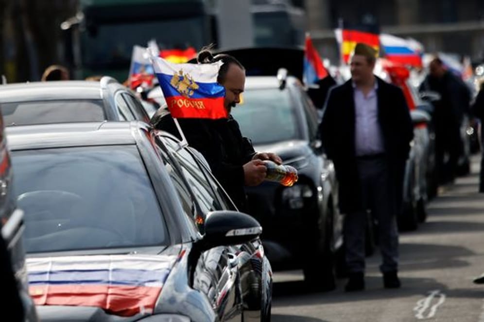 Flaggen mit den russischen Nationalfarben und dem russischen Staatswappen wehen an einem Auto auf dem Olympiaplatz vor dem Olympiastadion.
