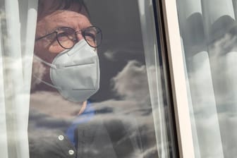 Mann mit FFP2-Maske hinter einer Fensterscheibe (Symbolbild): Corona-Infizierte müssen sich ab dem 1. Mai nicht mehr verpflichtend in Isolation begeben.