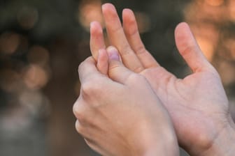 Frau fasst sich an Finger: Eine Arthrose in den Finger wird oft durch eine genetische Veranlagung hervorgerufen.
