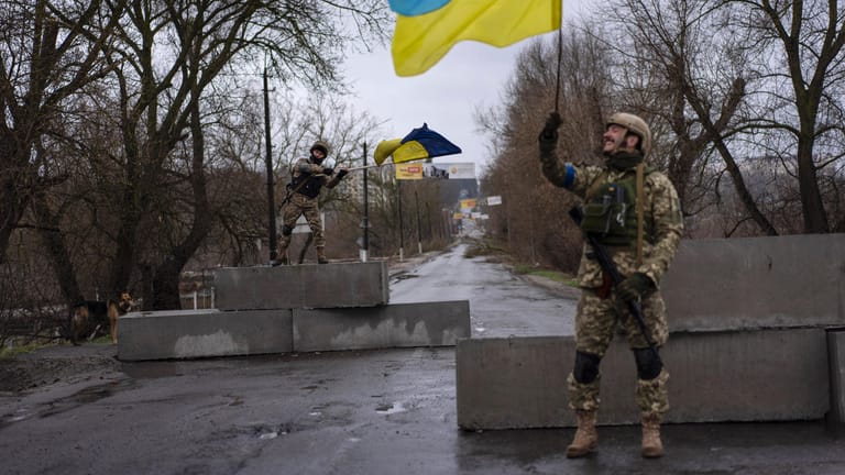 Butscha: Zwei ukrainische Soldaten stehen an einer Straßenblockade und halten ukrainische Fahnen hoch. Für die Ukraine sind die Gegenoffensiven wichtige moralische Erfolge.