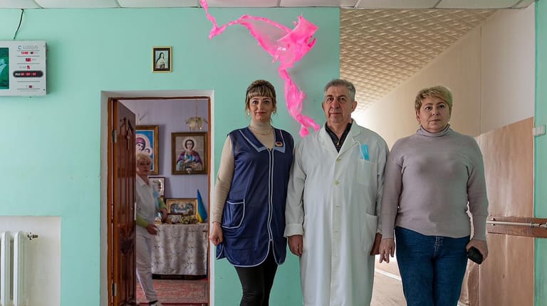 Olexandriya in der Ukraine: Pflegekraft Elena Viorika (l-r), der Direktor Vitali Sklarovskiy und die Krankenschwester Irina Lipobad stehen in einem Altenpflegeheim unter einer Installation des Künstlers Aljoscha.