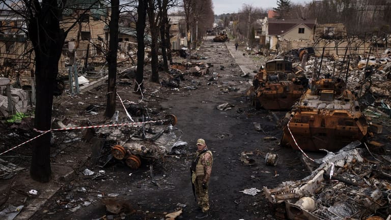 Ein ukrainischer Soldat steht in Butscha neben zerstörten russischen Panzern.