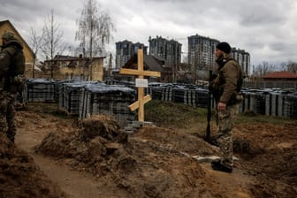 Ein ukrainischer Soldat steht neben einem Grab in Butscha: Laut dem BND planten russische Truppen offenbar den Mord an den Zivilisten per Funkspruch.