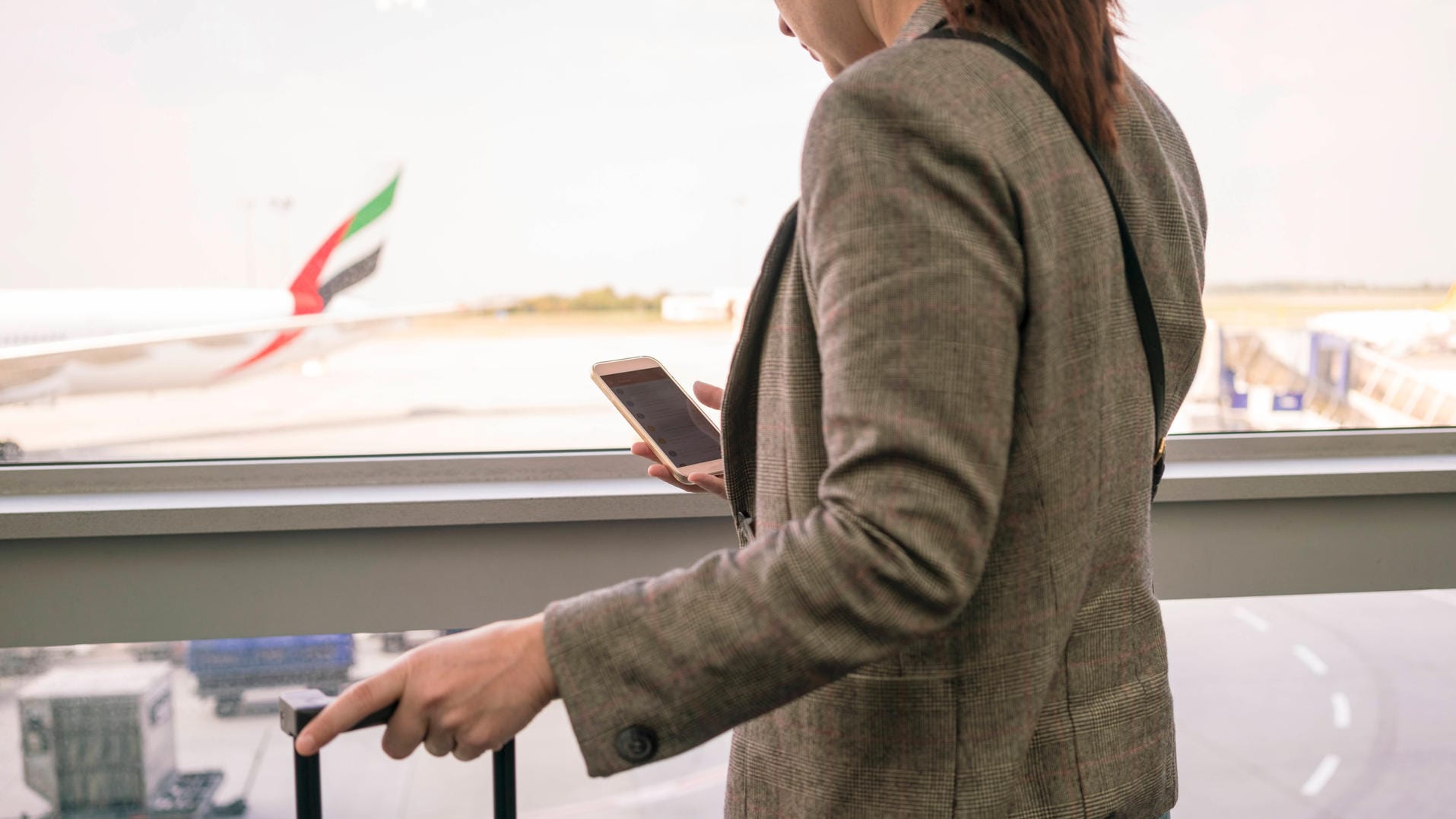 Woman at airport using smartphone with airplane in the background Budapest, Hungary ,model released, Symbolfoto PUBLICAT