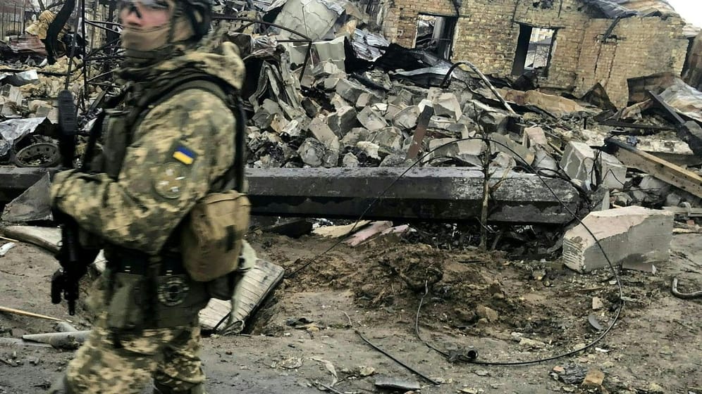 Ein ukrainischer Soldat läuft in Butscha an den Trümmern zerstörter Häusern vorbei.