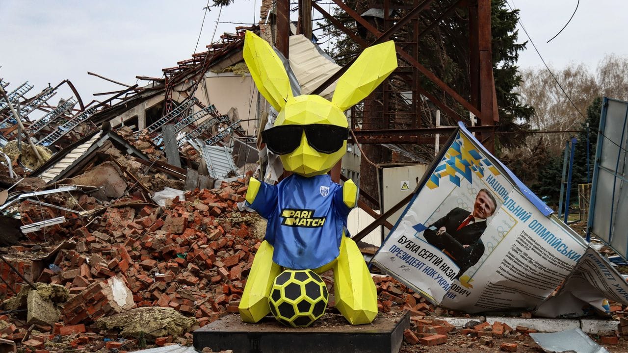 Ein Maskottchen steht vor einem zerstörten Gebäude auf dem Gelände des Sporttrainingszentrums in Tschernihiw.