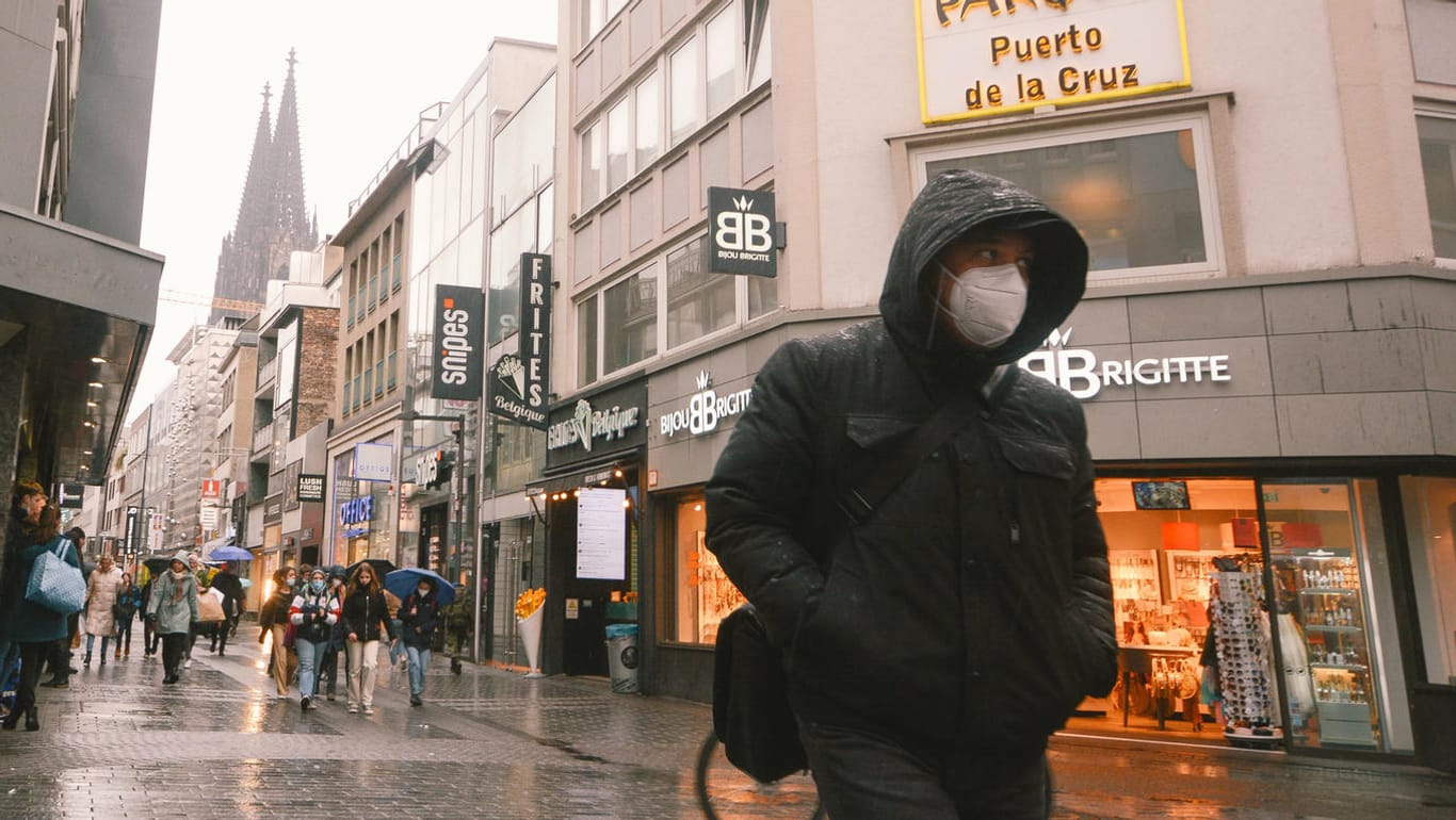 Ein Passant mit Maske läuft in der Kölner Innenstadt (Symbolbild): Experten raten trotz sinkender Zahlen zu Schutz in Innenräumen.