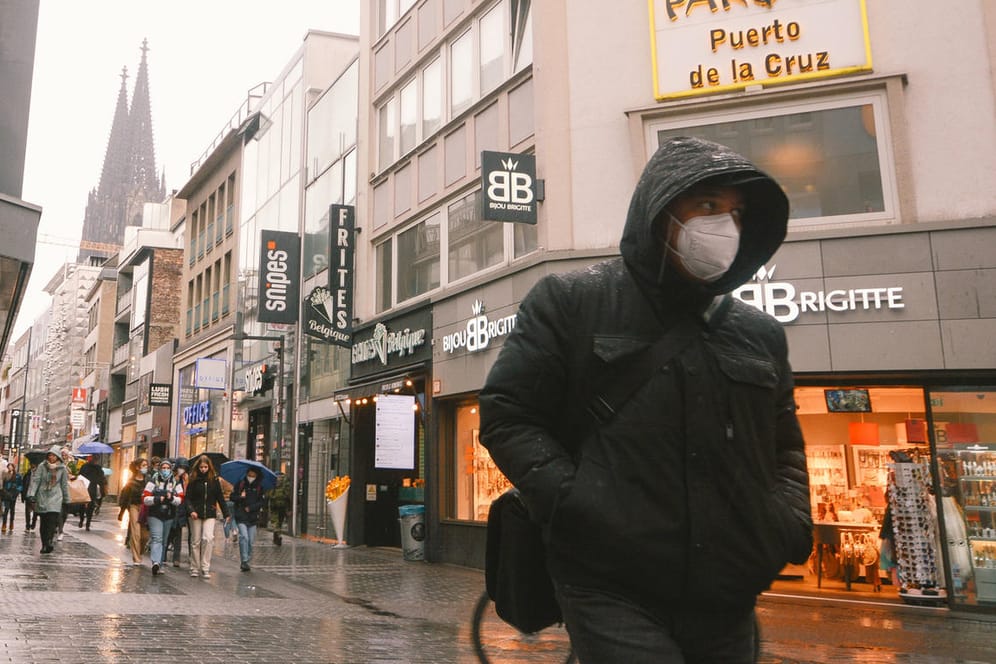 Ein Passant mit Maske läuft in der Kölner Innenstadt (Symbolbild): Experten raten trotz sinkender Zahlen zu Schutz in Innenräumen.