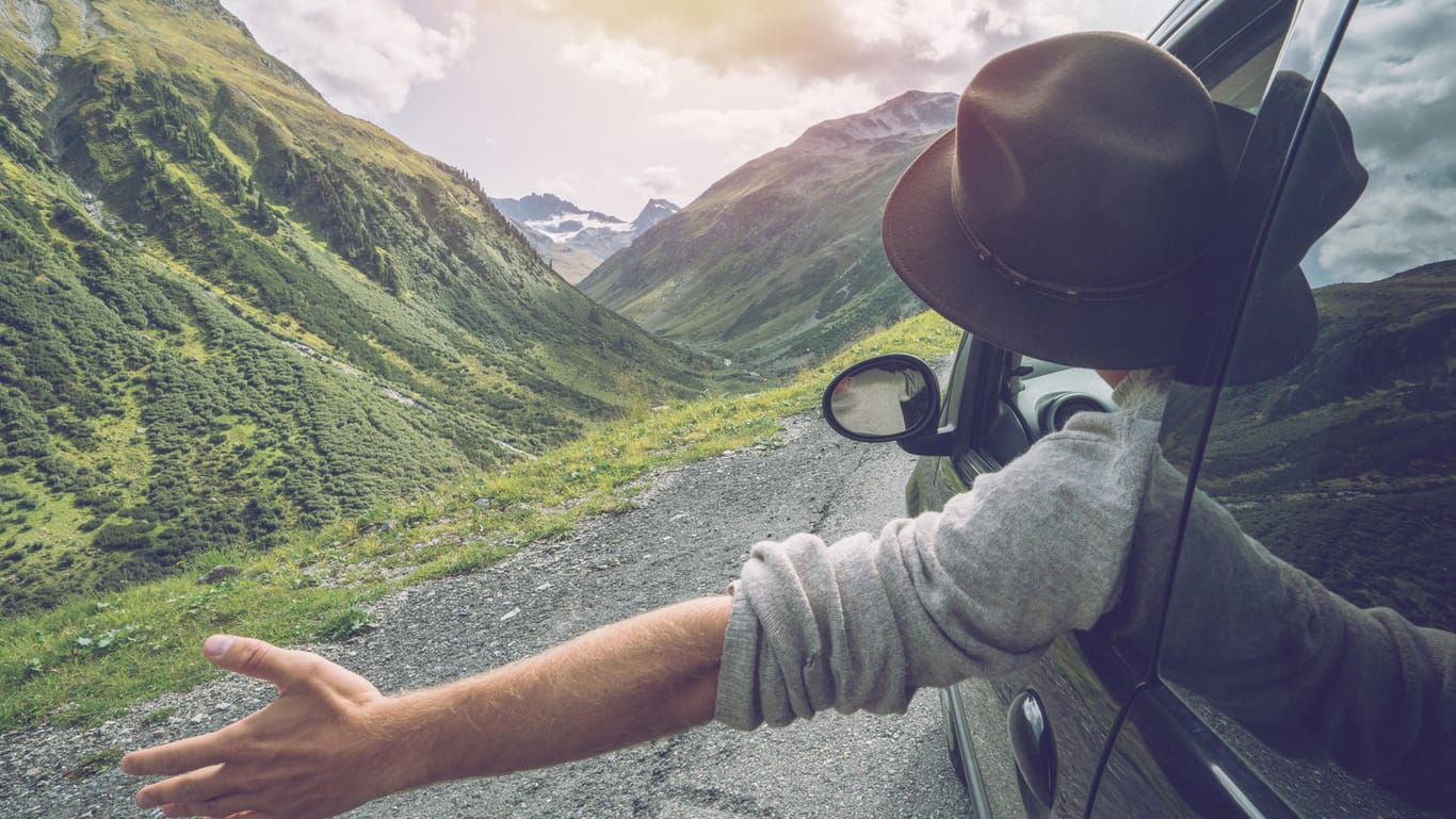 Eine Person fährt mit einem Auto durch die Berge: In einem Mietwagen lassen sich Urlaubsorte bequem erkunden.