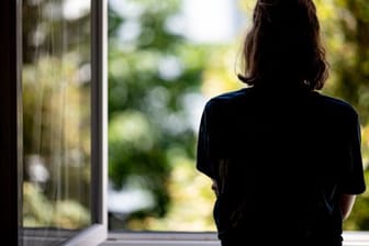 Eine Frau steht in ihrer Wohnung an einem Fenster (Symbolbild): Häusliche Gewalt nimmt an Feiertagen zu.