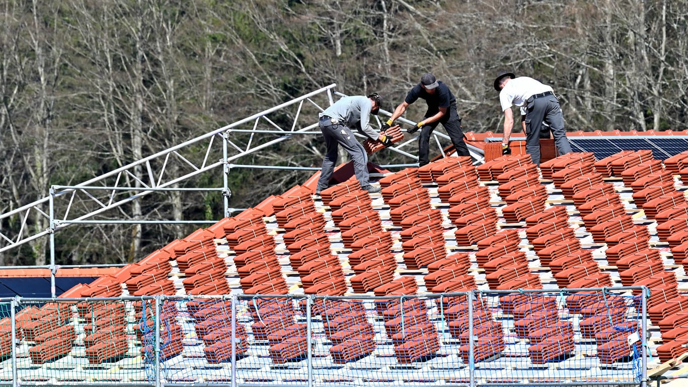 Dachdecker bestücken einen Rohbau mit Ziegeln (Symbolbild): Bauen wird aktuell immer teurer, nun steigen auch die Preise für Dachziegel. hland *** Soon the roof wi