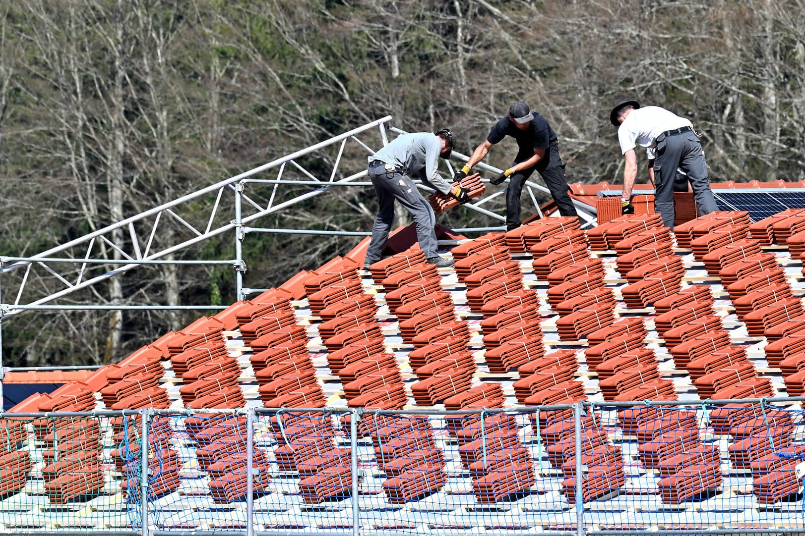 Dachdecker bestücken einen Rohbau mit Ziegeln (Symbolbild): Bauen wird aktuell immer teurer, nun steigen auch die Preise für Dachziegel. hland *** Soon the roof wi