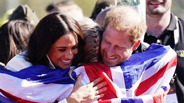 Prinz Harry (r) und Meghan (l) umarmen die britische Teilnehmerin Lisa Johnston.