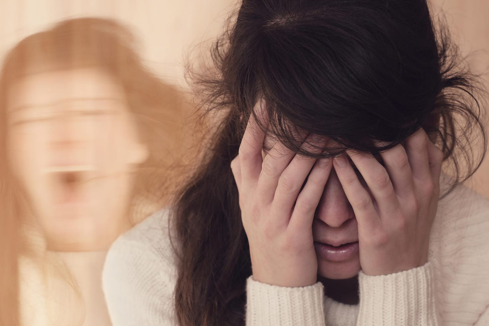 Junge Frau hält sich die Augen zu, im Hintergrund der Schatten einer schreienden Frau.