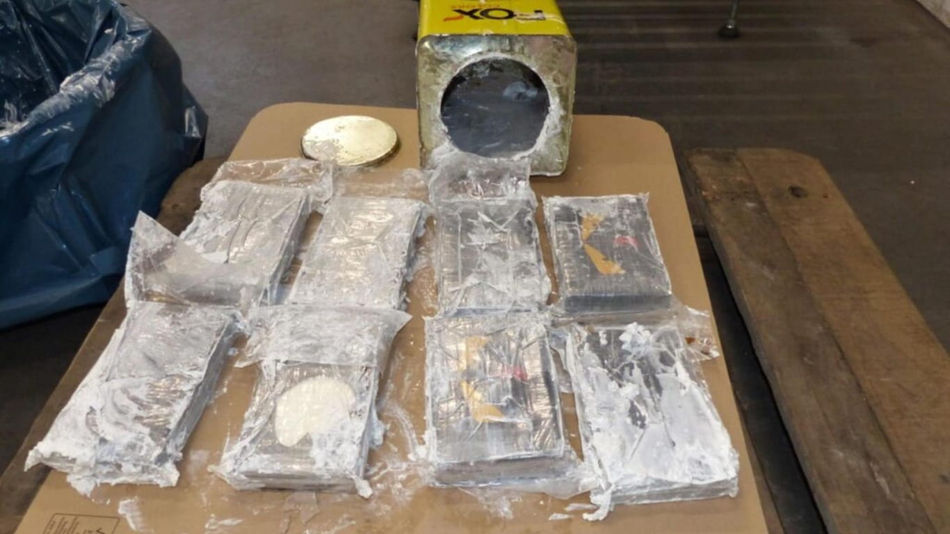 Drogenpakete und eine geöffnete Blechdose liegen auf einem Tisch (Archivbild): Im Februar 2021 war versucht worden, auf diese Weise 16 Tonnen Kokain über den Hamburger Hafen einzuschmuggeln.