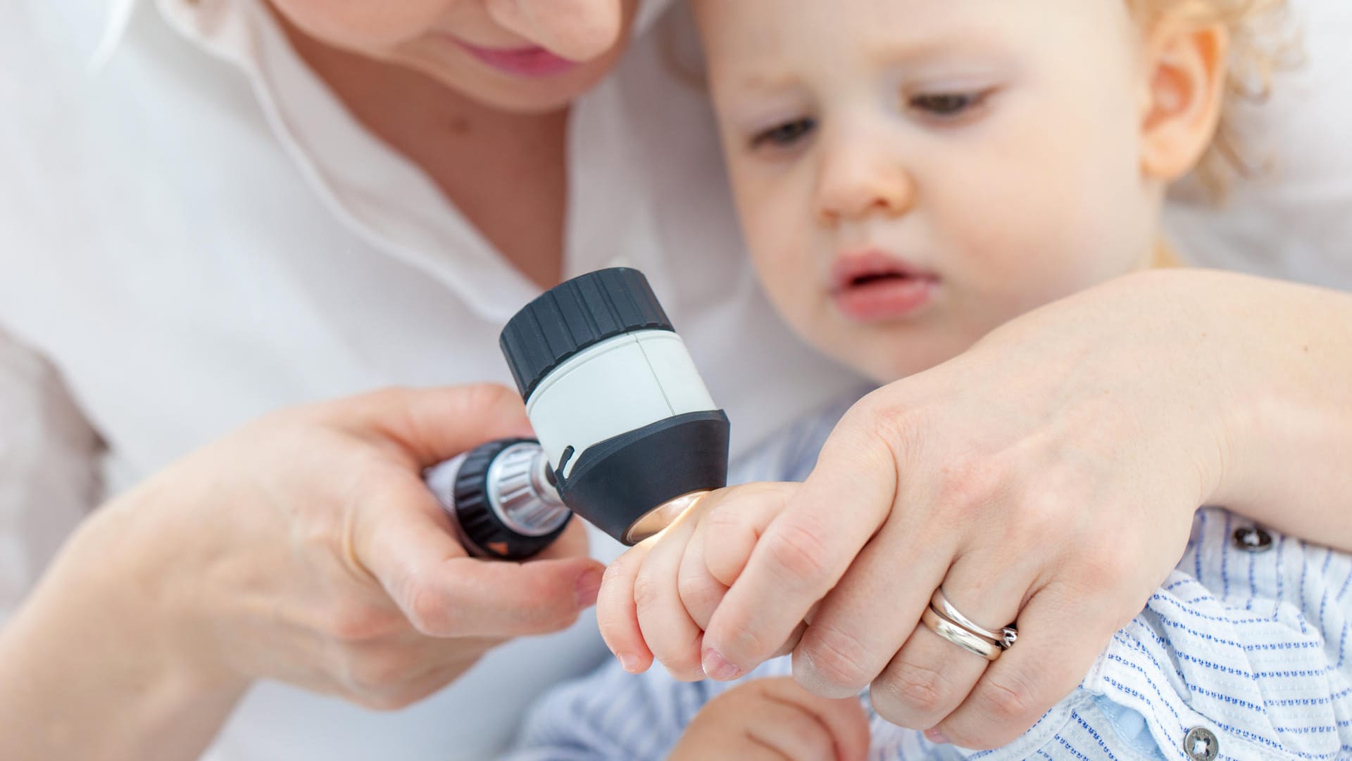 Eine Ärztin untersucht die Hand eines Kleinkinds mit einem Dermatoskop