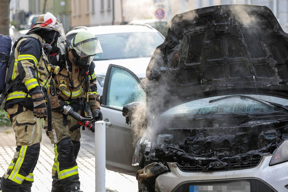 Zwei Löschkräfte der Feuerwehr vor einem Auto (Symbolfoto): In Berlin dauerte ein Löscheinsatz der Feuerwehr stundenlang an.