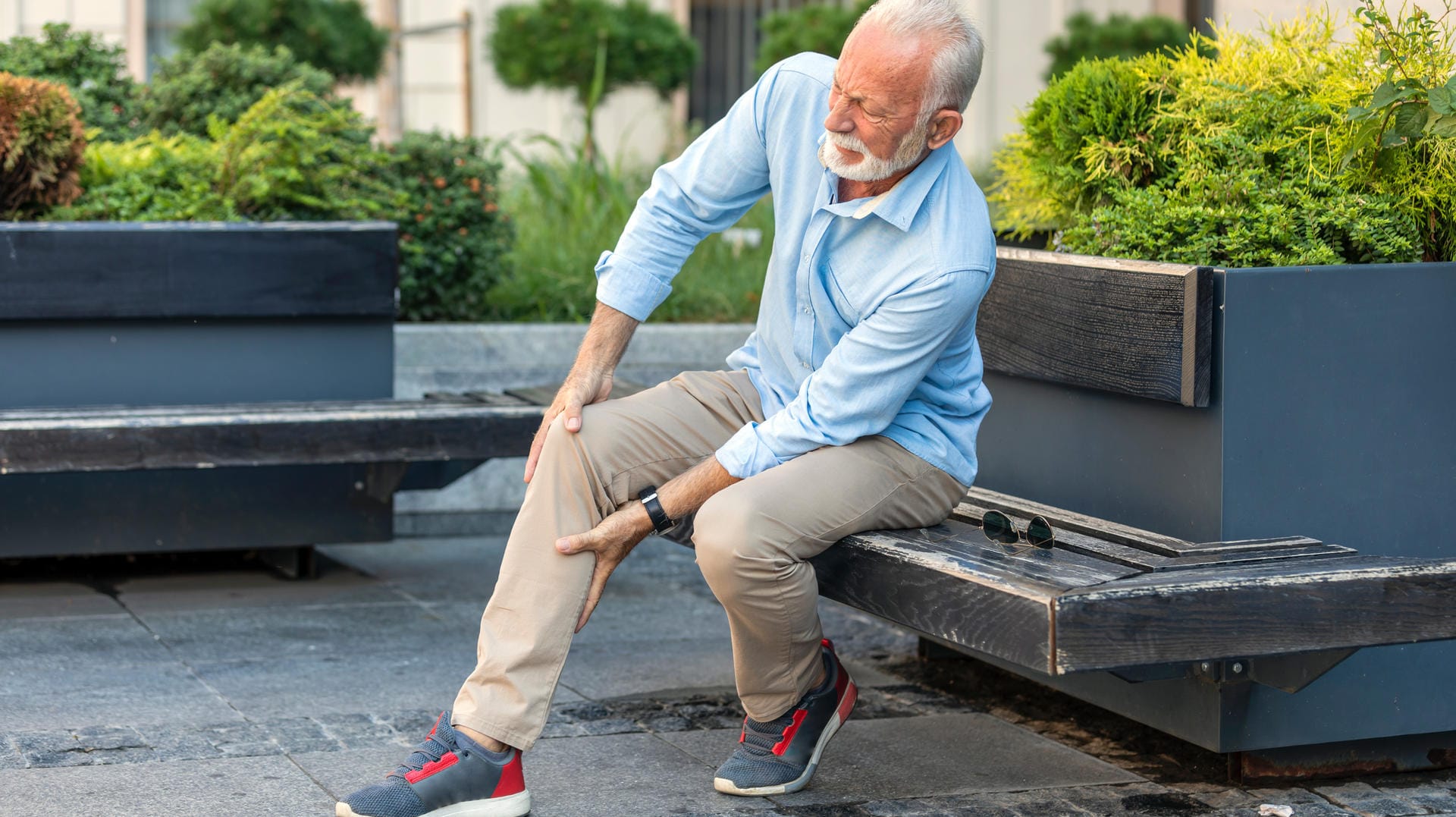 Mann mit Beinschmerzen sitzt auf Bank.