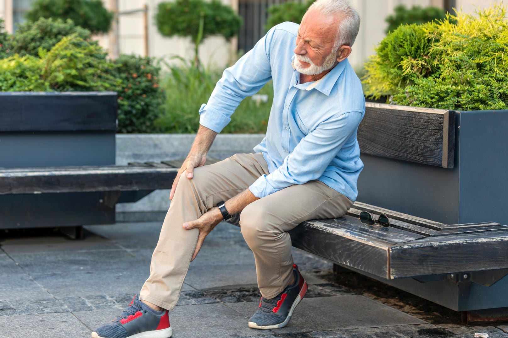 Mann mit Beinschmerzen sitzt auf Bank.