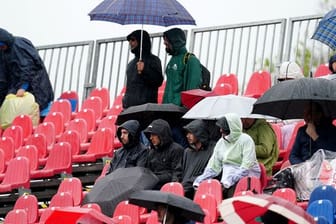 Fans sitzen während des Freien Trainings mit Regenschirmen auf der Tribüne.
