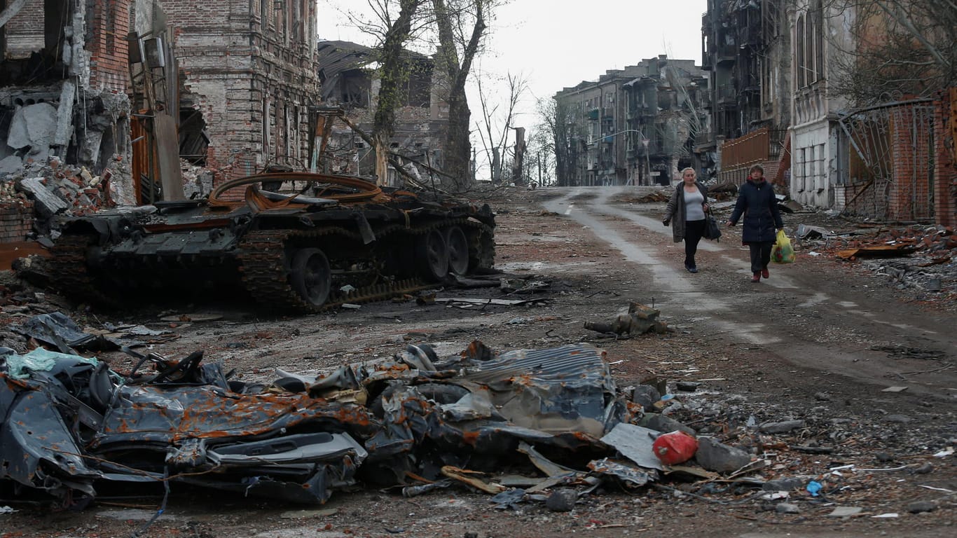 Einwohner Mariupols laufen an zerstörtem Kriegsgerät vorbei.