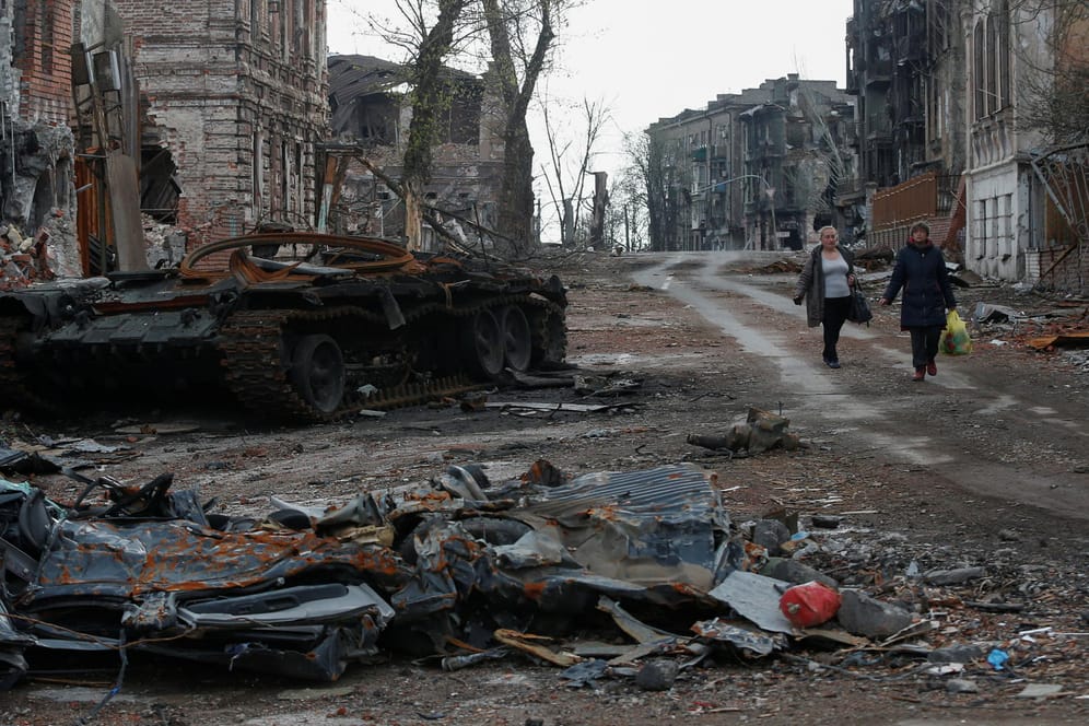 Einwohner Mariupols laufen an zerstörtem Kriegsgerät vorbei.