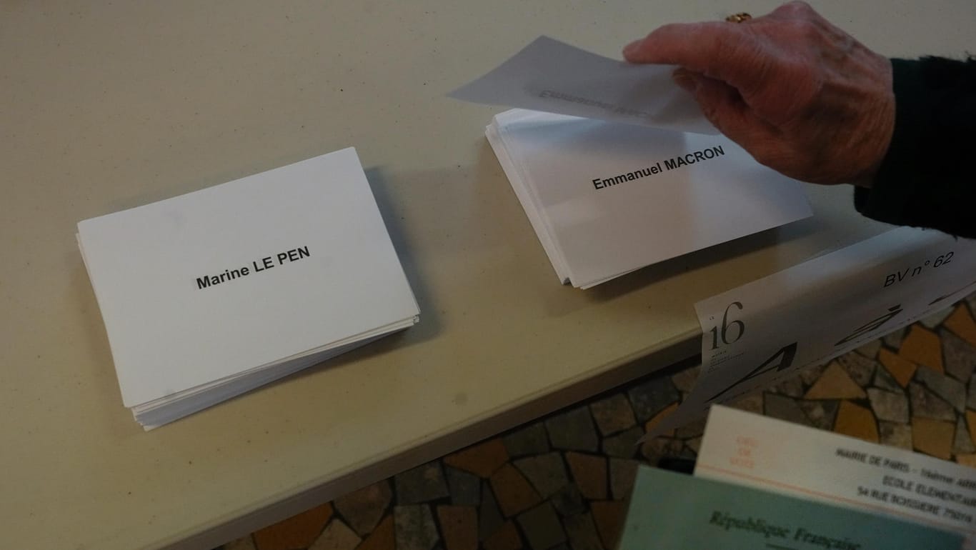 Ein Wähler greift nach den Wahlzetteln: In Frankreich kreuzen die Wähler nicht wie in Deutschland Felder auf einem Wahlzettel an, sondern nehmen Papiere mit den Namen der Kandidaten oder einer "Enthaltung" mit in die Kabine.