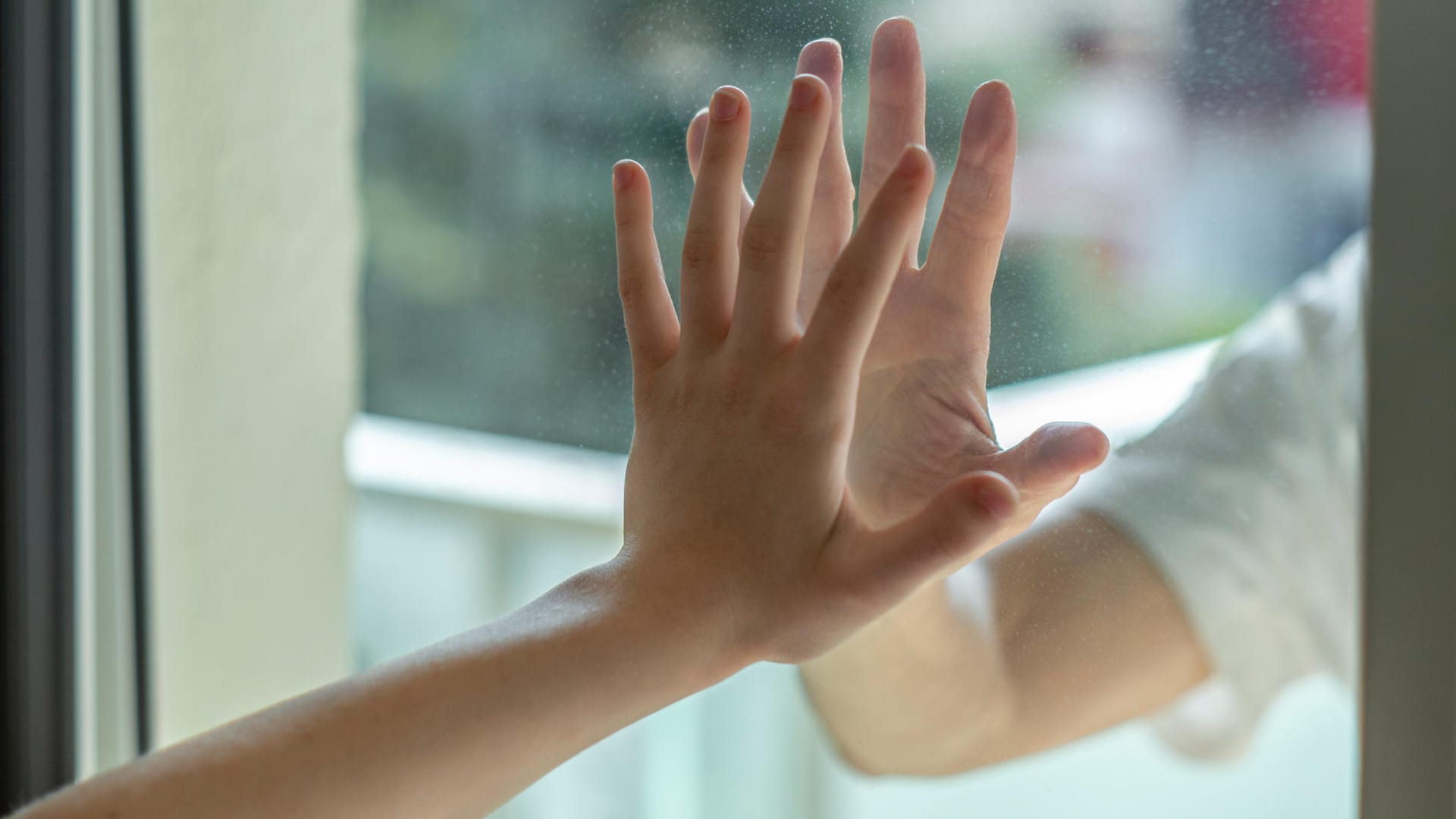 Zwei durch eine Glasscheibe getrennte Hände