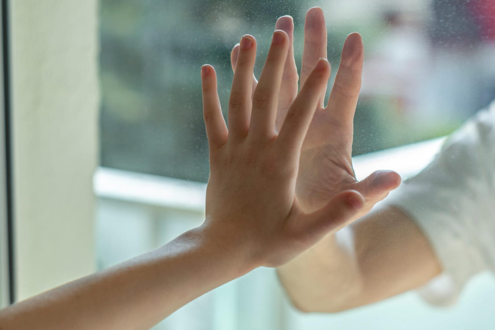 Zwei durch eine Glasscheibe getrennte Hände