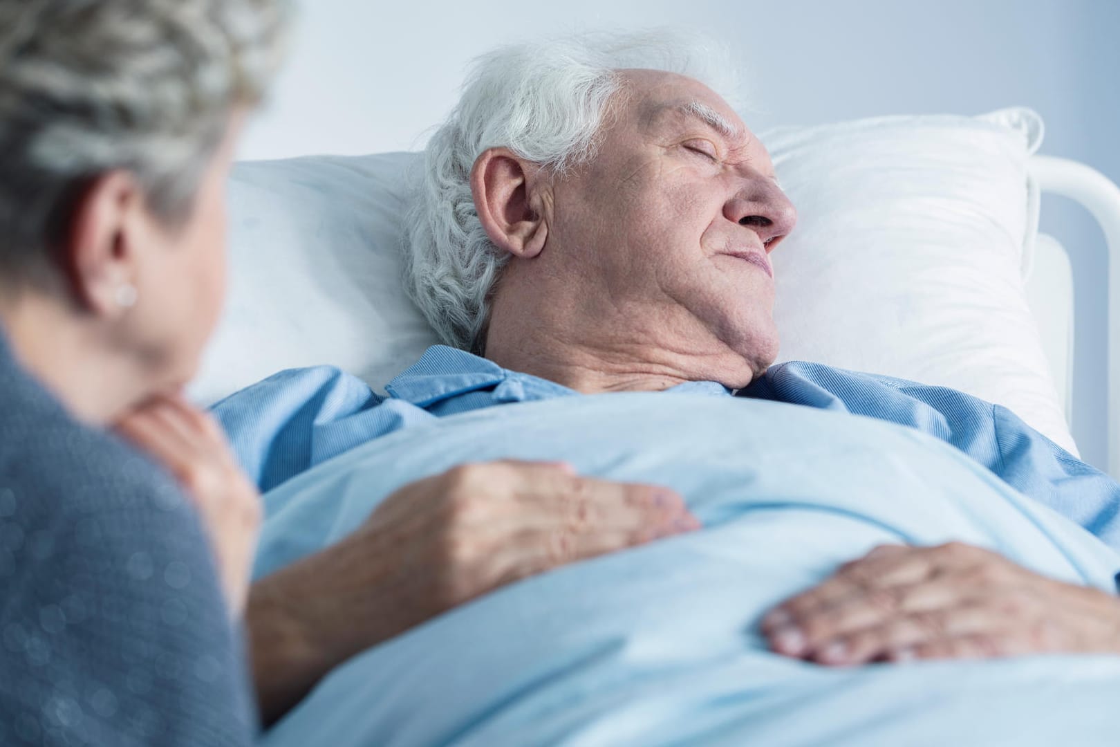 Eine Frau sitzt am Krankenbett ihres Mannes.