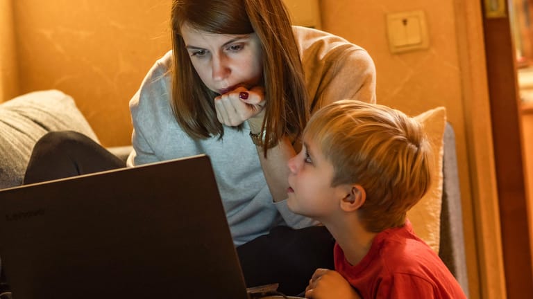 Eine Frau arbeitet am Laptop, während ein kleiner Junge sie anspricht (Symbolbild): Berufstätigkeit und Kinderbetreuung zu vereinen, stellt gerade für junge Familien eine Herausforderung dar.