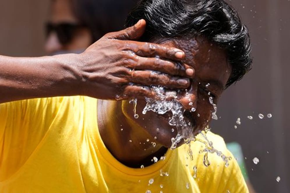 Ein Mann spritzt sich an einem extrem heißen Tag auf einem Marktplatz in Mumbai Wasser ins Gesicht.