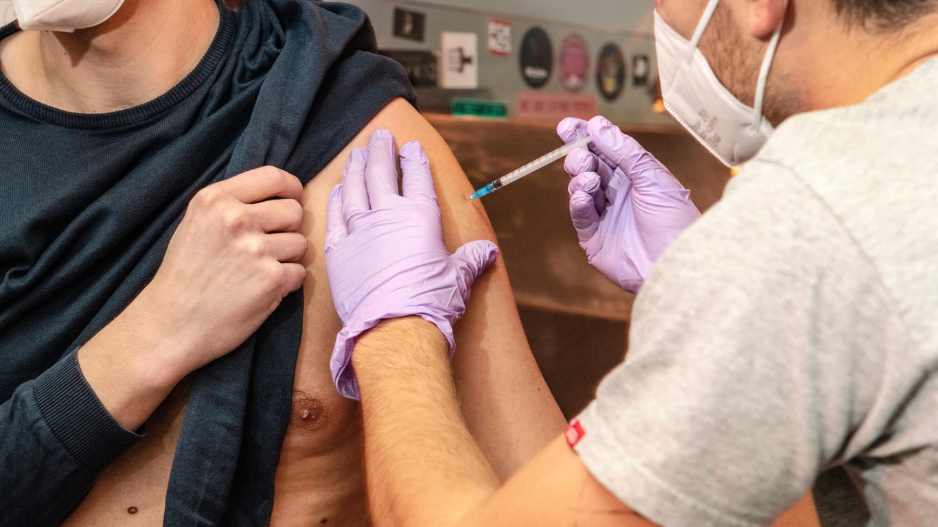Ein Arzt selbst eine Spritze in den Oberarm eines jungen Mannes (Symbolbild): in Deutschland sind nur zwei Drittel dreimal geimpft.