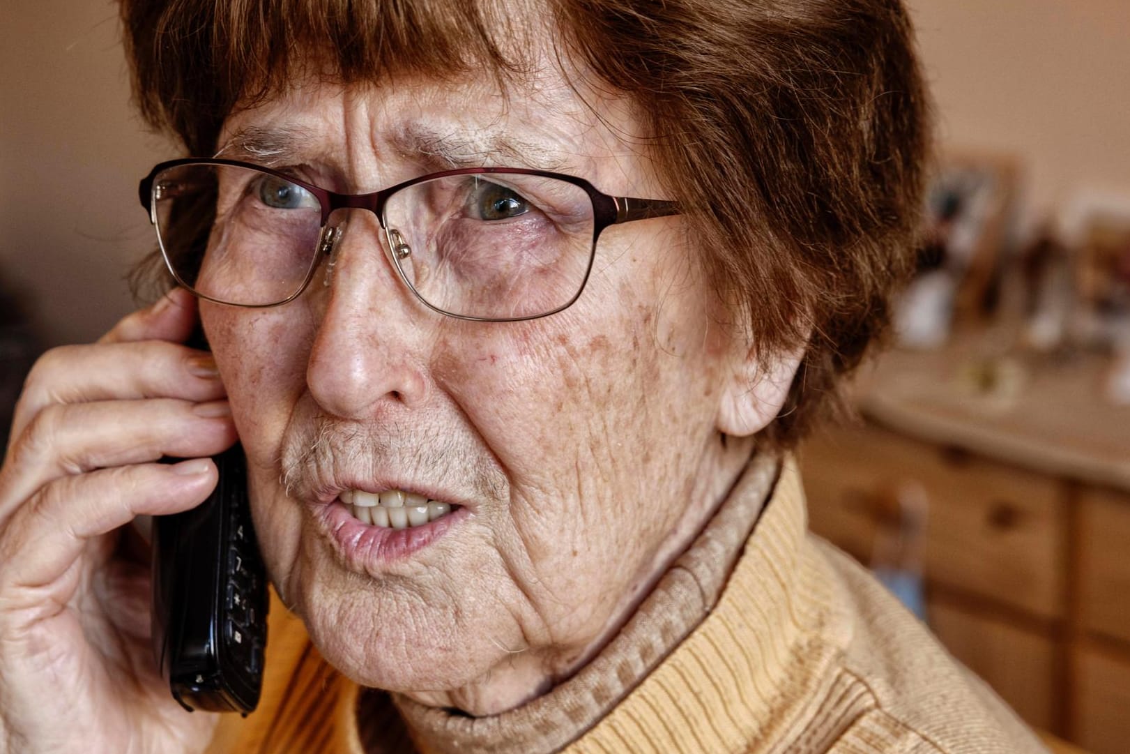 Seniorin zuhause beim Telefonieren schaut unsicher (Symbolbild): Neben dem Enkeltrick gibt es auch zahlreiche andere Maschen, die mittlerweile durch professionelle Call-Centren ausgeführt werden.