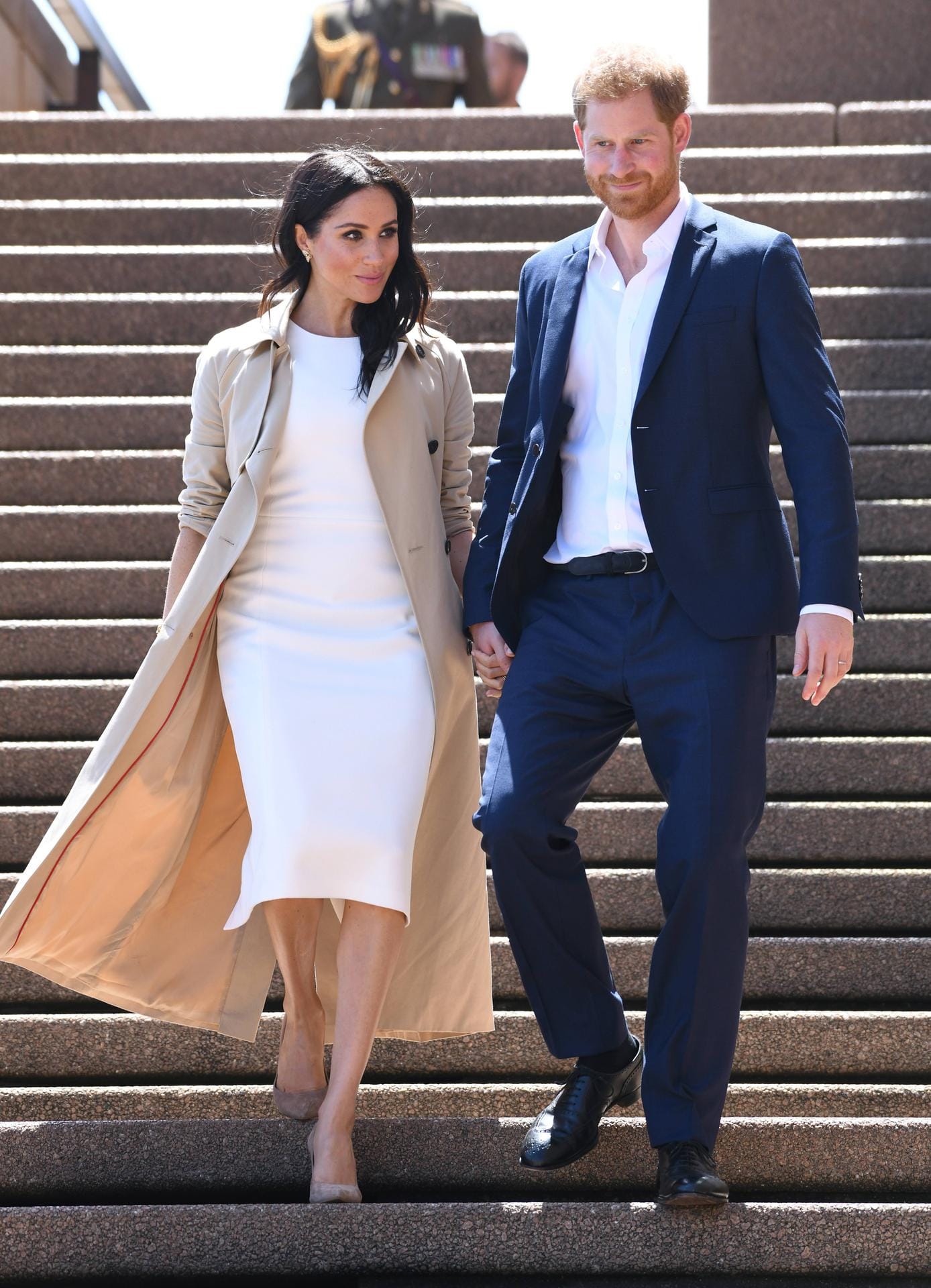 Angekommen in Sydney folgt der erste Auftritt nach Verkündung der Schwangerschaftsnews: Meghan in einem weißen Kleid der australischen Designerin Karen Gee, kombiniert mit einem beigefarbenen Mantel.
