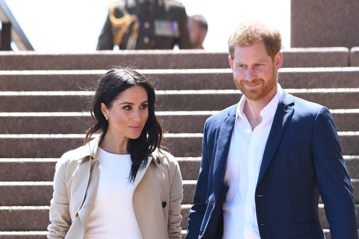 Angekommen in Sydney folgt der erste Auftritt nach Verkündung der Schwangerschaftsnews: Meghan in einem weißen Kleid der australischen Designerin Karen Gee, kombiniert mit einem beigefarbenen Mantel.