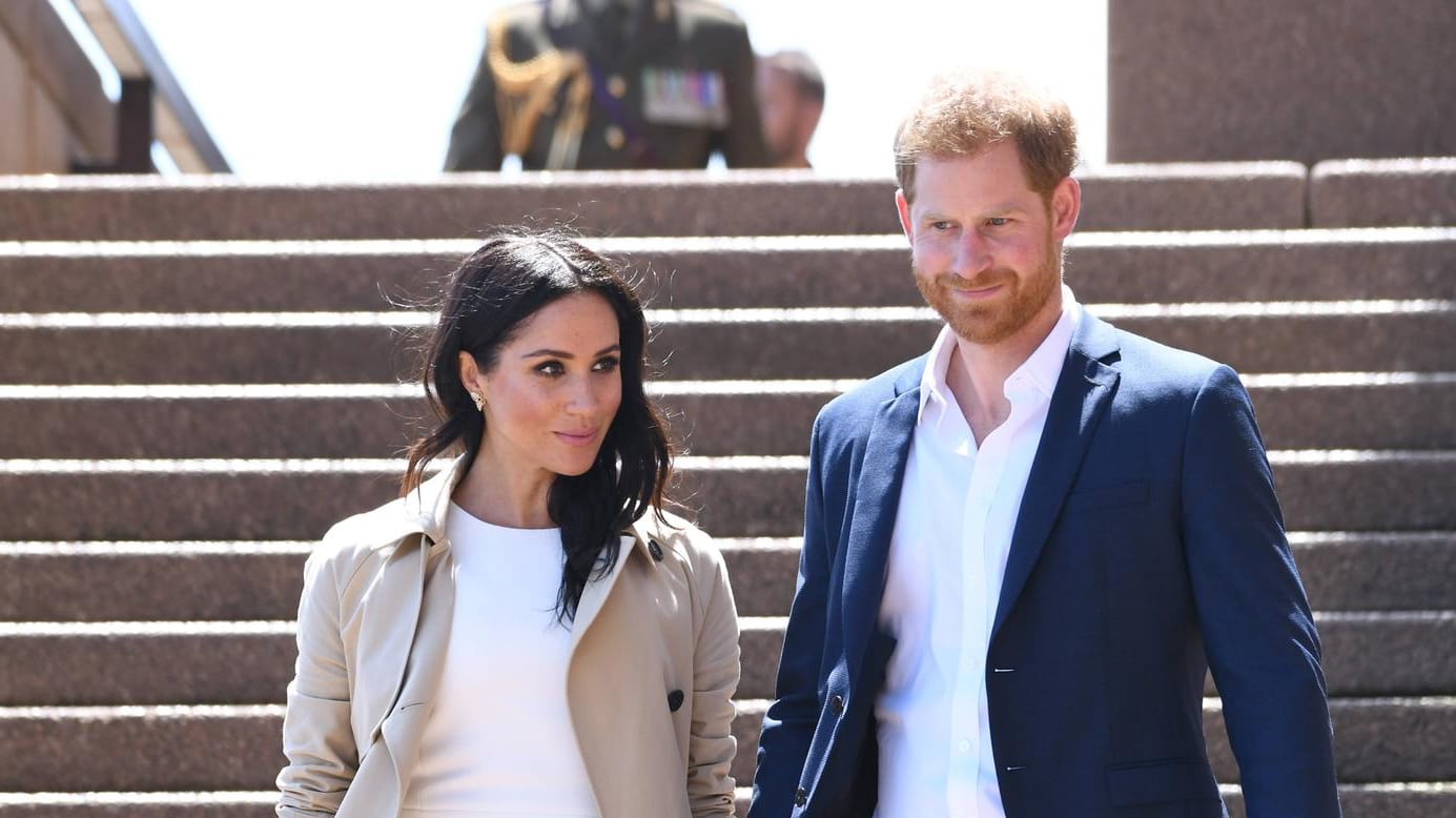 Angekommen in Sydney folgt der erste Auftritt nach Verkündung der Schwangerschaftsnews: Meghan in einem weißen Kleid der australischen Designerin Karen Gee, kombiniert mit einem beigefarbenen Mantel.