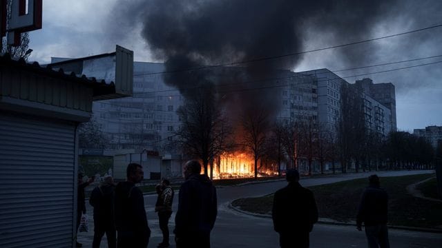 Anwohner stehen vor ihren Wohnungen in Charkiw, während Geschäfte nach einem russischen Angriff brennen.