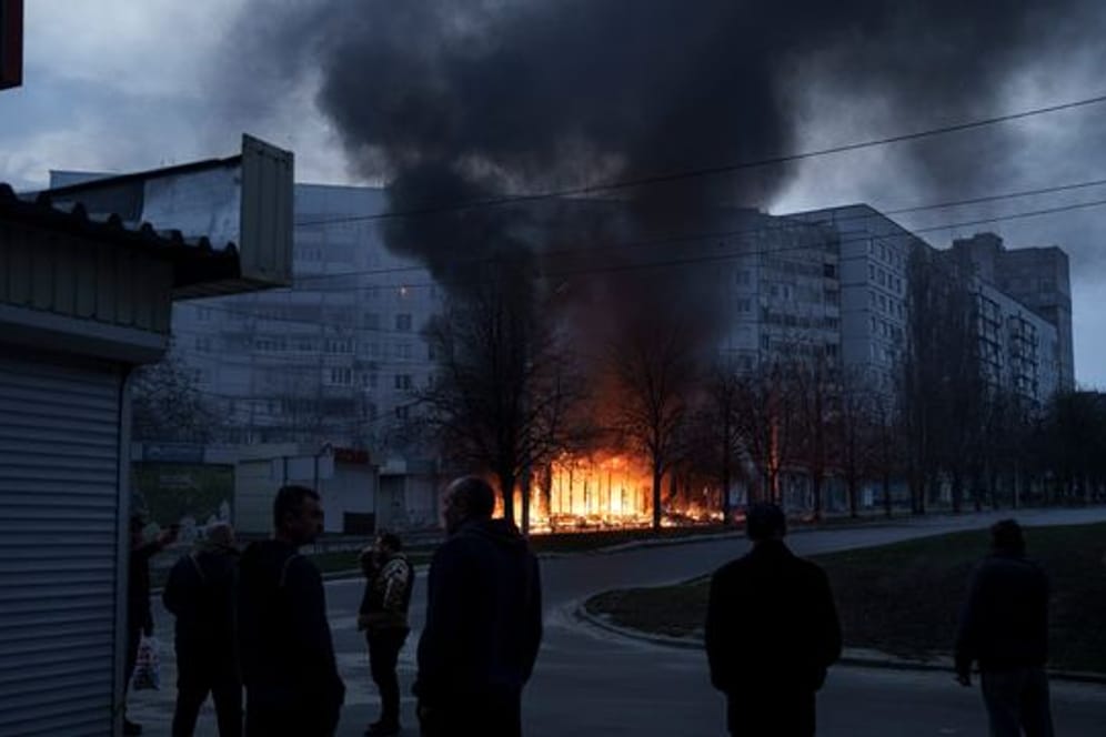 Anwohner stehen vor ihren Wohnungen in Charkiw, während Geschäfte nach einem russischen Angriff brennen.