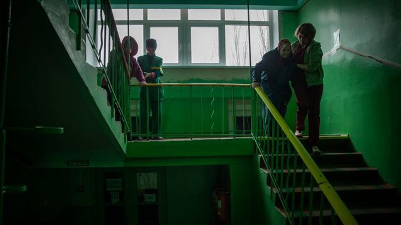 Arbeiter helfen den Bewohnern eines Altenheims bei der Evakuierung aus dem ukrainischen Toretsk über eine Treppe.