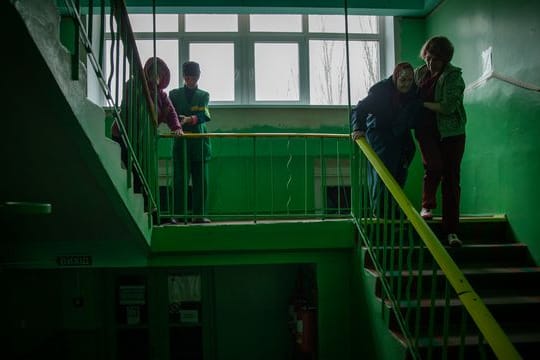 Arbeiter helfen den Bewohnern eines Altenheims bei der Evakuierung aus dem ukrainischen Toretsk über eine Treppe.