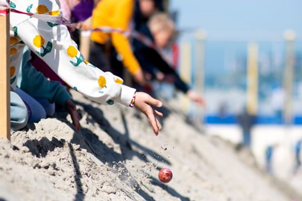 Kinder lassen am Ostersonntag bunte Eier von einer aufgeschütteten Düne am Weststrand von Norderney heruntertrullern.