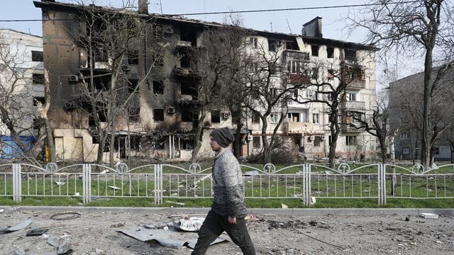 Ein Mann geht in der Nähe eines durch Beschuss zerstörten Wohnhauses in Mariupol.