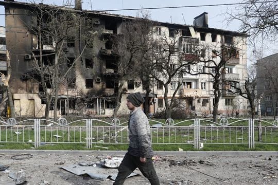 Ein Mann geht in der Nähe eines durch Beschuss zerstörten Wohnhauses in Mariupol.