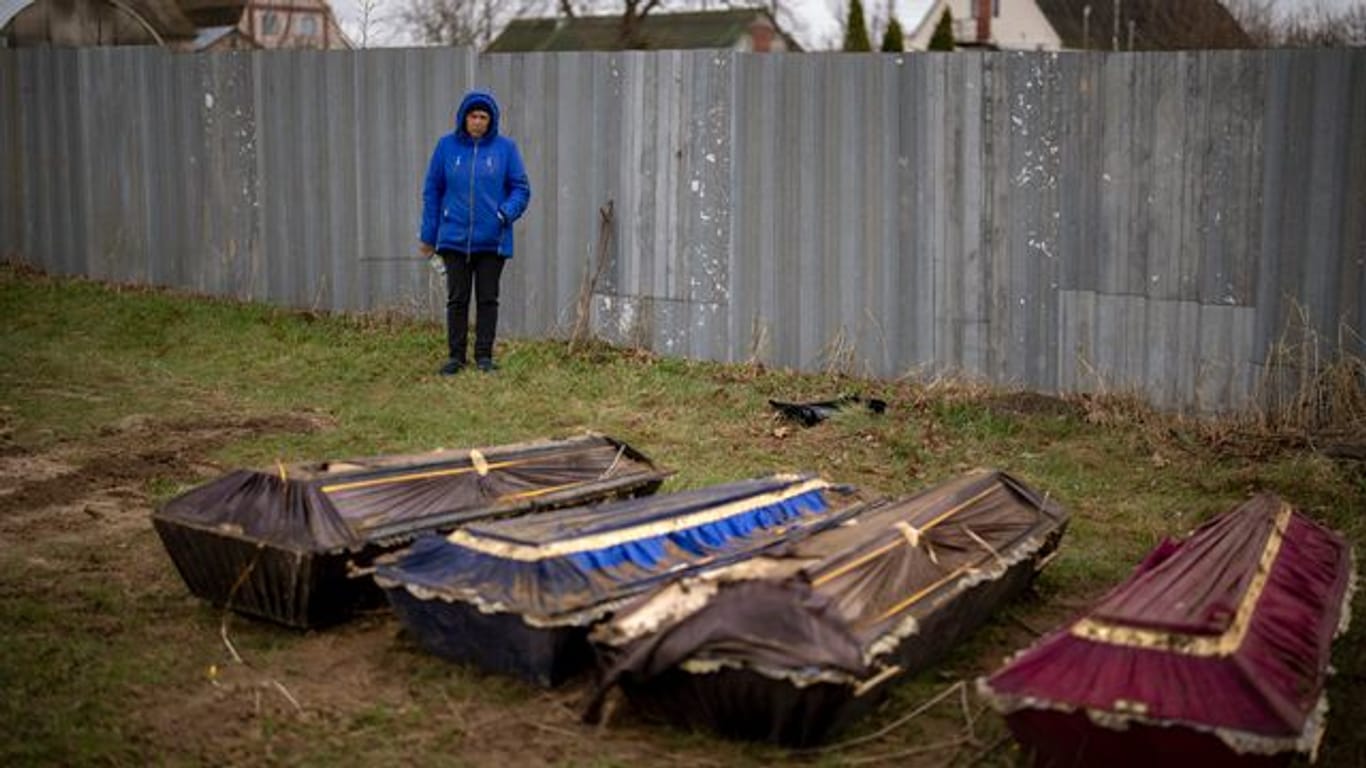 Eine Frau steht während der Exhumierung eines Massengrabes neben Särgen in Butscha.